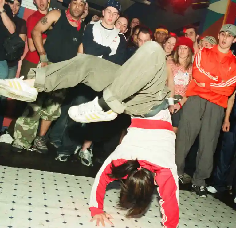 A breakdancer shows off their moves while other dancers watch on from the sidelines.